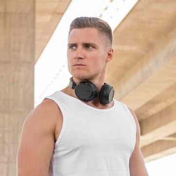 Man wearing a white tank top and black headphones with a blurred architectural background