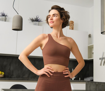 Yoga Woman Pilates Mom in a brown sports bra and leggings standing in a modern kitchen ready to start the day with some saenatree gummies